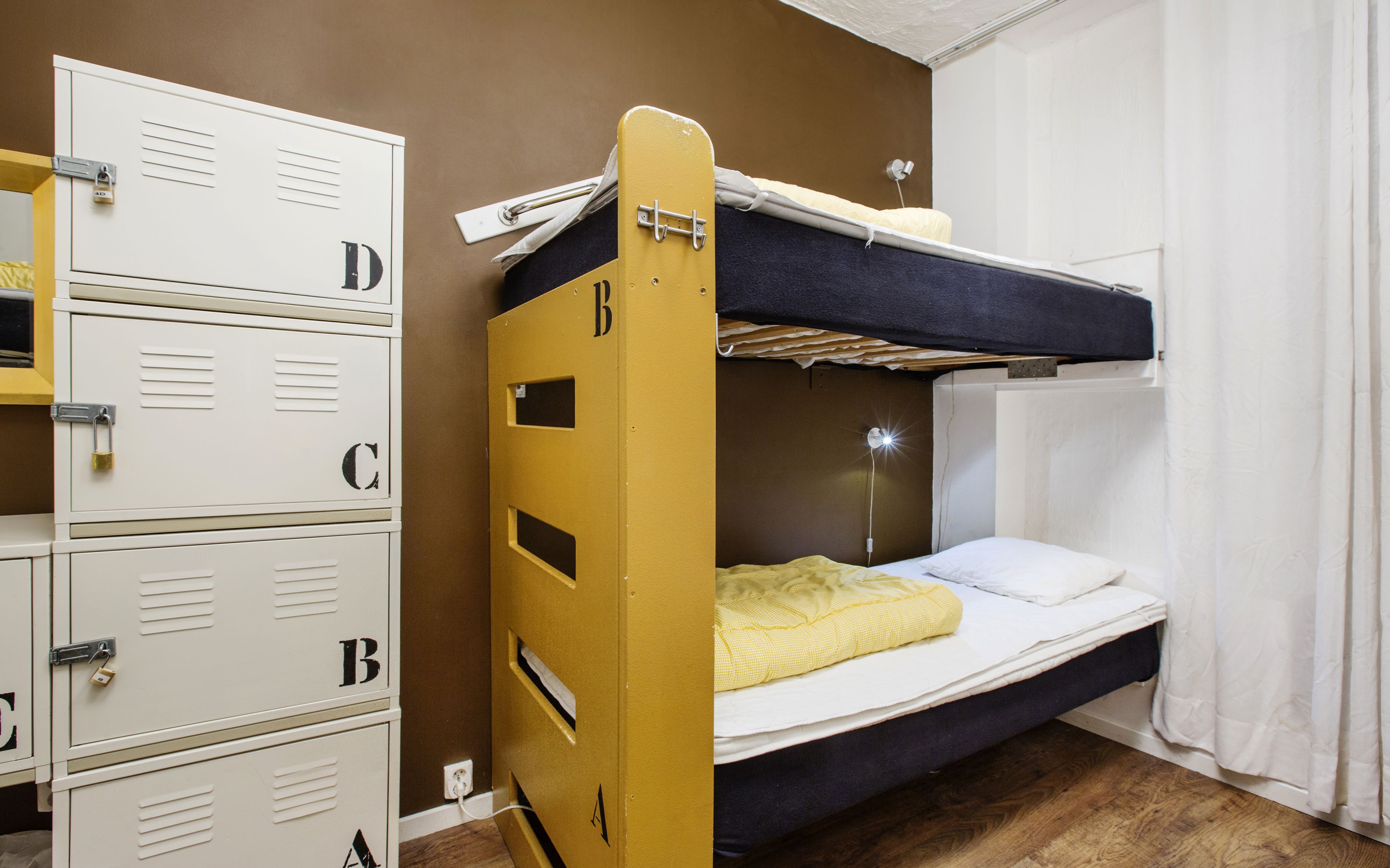 A bunk bed with a yellow ladder, a white mattress, and a yellow blanket. There are white lockers with letters on them.