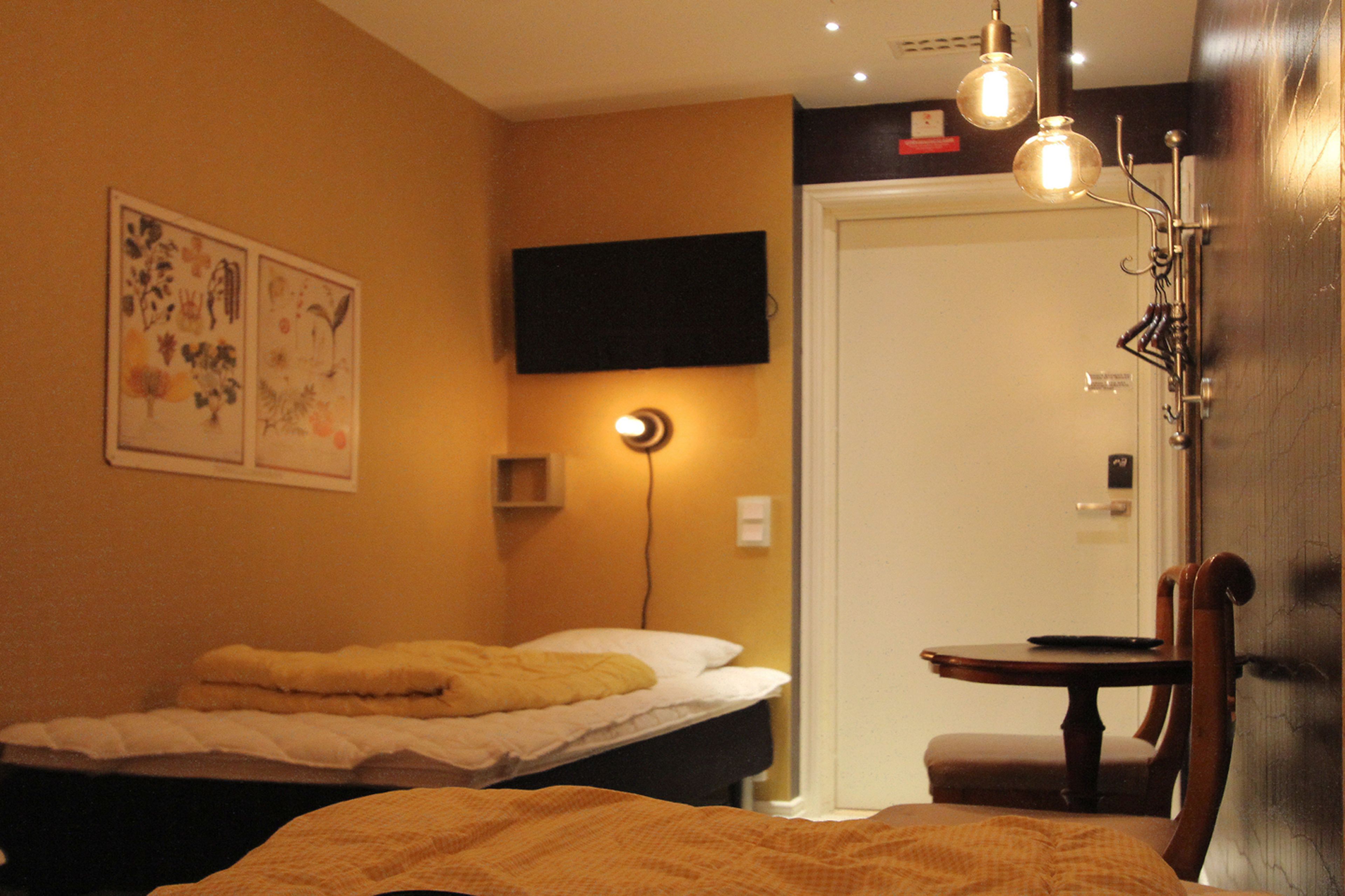 A hotel room with a bed, a bedside table, a chair, a wall-mounted TV, and a door.