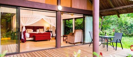 Una villa moderna con un amplio ventanal que da a un dormitorio con sofá rojo y cama con dosel.