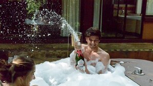 Une personne dans une baignoire remplie de mousse, tenant une bouteille de champagne.