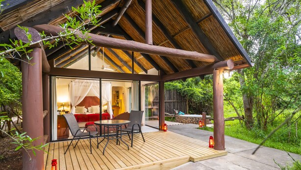 Une terrasse en bois dotée d’une enceinte en verre, d’un coin repas et d’un espace salon confortable avec des coussins.