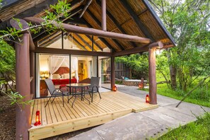 A wooden deck with a glass enclosure, a dining area, and a cozy seating space with cushions. - Leopard Walk Lodge (Hluhluwe)