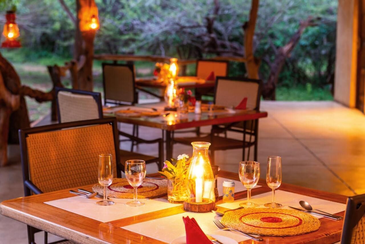 An outdoor dining area with wooden tables, chairs, and a central candle centerpiece.