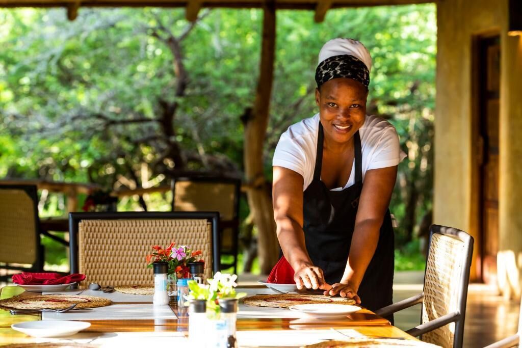 A person preparing food at an outdoor dining table with a natural backdrop.