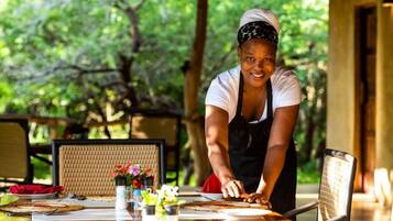 A person preparing food at an outdoor dining table with a natural backdrop.