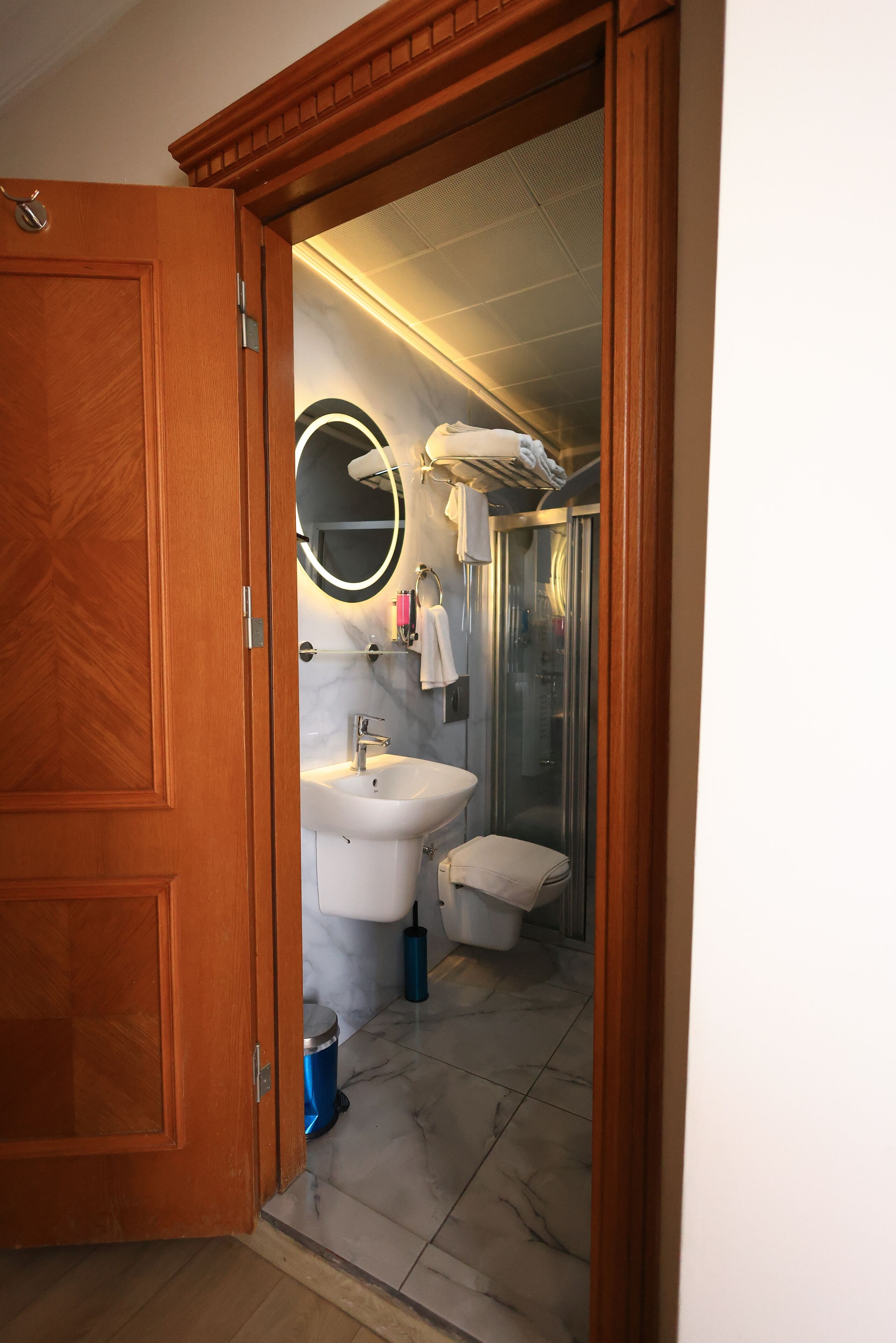 A bathroom with a wooden door, a sink, a mirror, a toilet, and a shower.