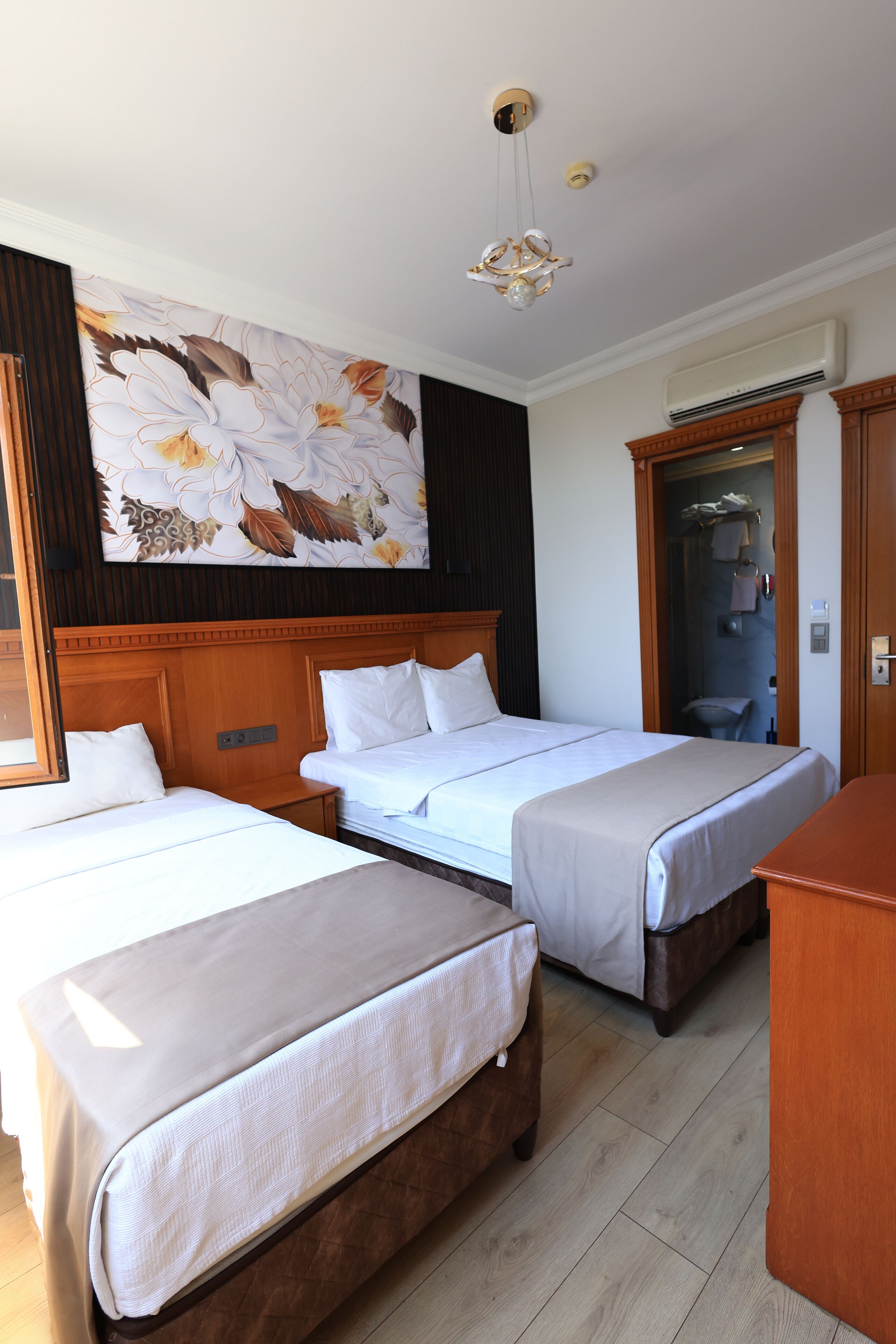Une chambre d’hôtel avec deux lits simples, une tête de lit en bois, une grande œuvre d’art florale accrochée au mur et un plancher en bois.