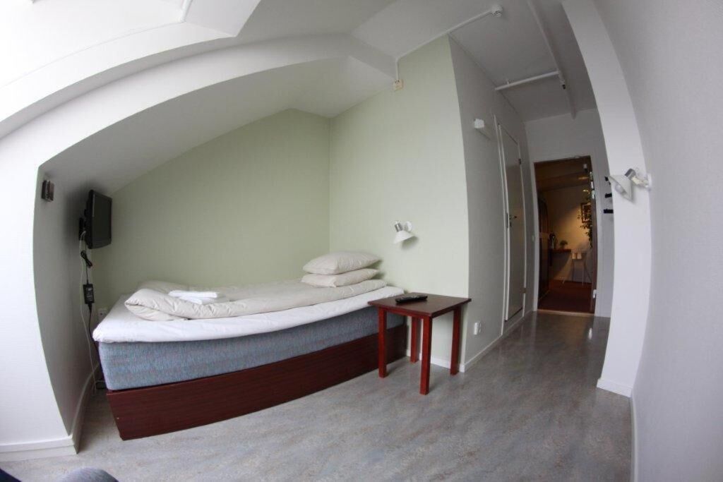 A compact room with a bed, a small table, and a wall-mounted lamp.
