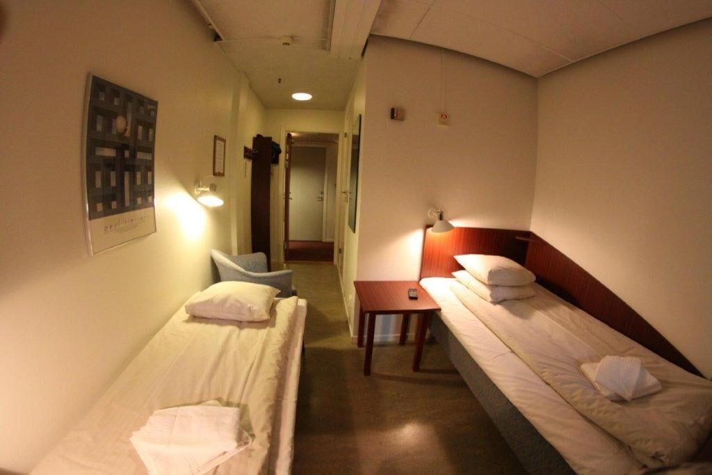 A hotel room with two single beds, a small table, and a chair.