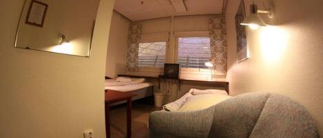 A compact bedroom with a bed, a chair, a desk, and a window.