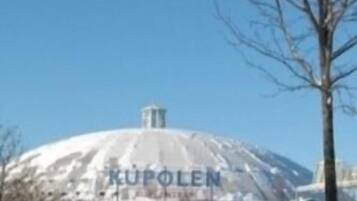 A snow-covered dome structure with the text "KUPOLEN" visible, surrounded by bare trees and a clear sky.