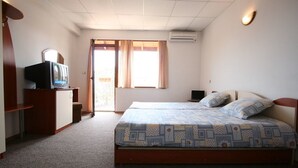 A bedroom with a bed, a television on a wooden cabinet, a small desk, and a window with curtains. - Kirios (Nessebar)