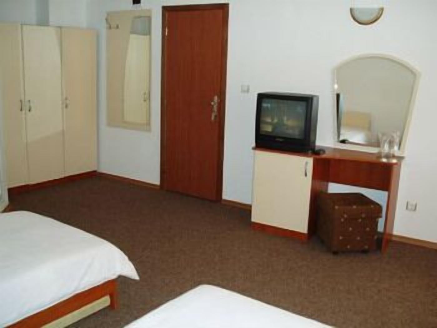 A hotel room with a bed, a desk with a television, a mirror, and a wardrobe.