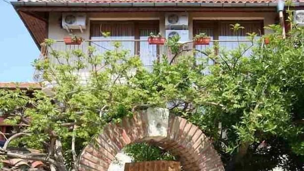 A traditional stone building with a wooden archway entrance, a balcony with potted plants, and a clear sky. - Kirios (Nessebar)