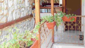 A covered balcony with wooden beams and stone walls, featuring potted plants and a view of a bar area with shelves of bottles. - Kirios (Nessebar)