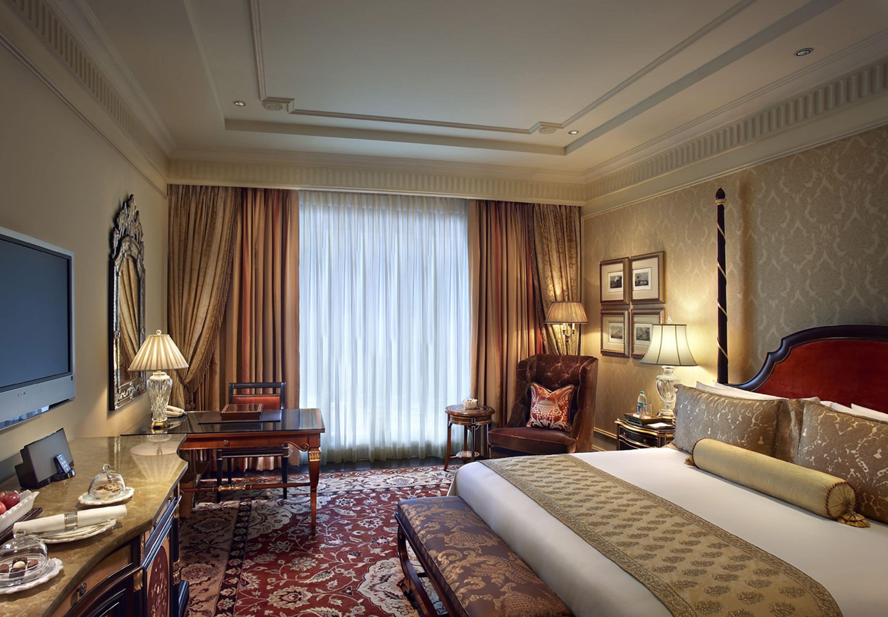 A hotel room with a large bed, a desk with a chair, a television, and a window with curtains.