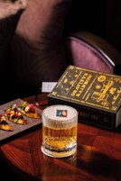 Un vaso de cerveza sobre una mesa de madera, con un libro titulado "Gravity's Rainbow" al fondo.