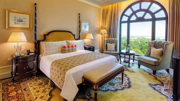 A hotel room with a large bed, a bench, two armchairs, a view of the outdoors, and a large window.