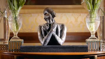 A statue of a man in a thoughtful pose, flanked by two vases with green plants, on a wooden table with a black marble top.