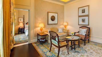 A well-appointed hotel room with a large bed, a sitting area with a sofa and armchairs, a small table with a vase, and two framed pictures on the wall.