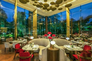 A modern restaurant with glass walls, red chairs, and a central dining area with round tables.