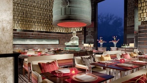 A restaurant with a traditional Asian design, featuring a large hanging bell, a Buddha statue, and a view of the night sky through a large window. - The Leela Palace New Delhi (New Delhi)