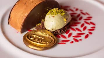 A dessert plate with a chocolate dome, a scoop of ice cream, and a decorative nut piece.