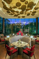 Zona pranzo moderna con tavoli rotondi, sedie imbottite rosse e un design di soffitto originale.
