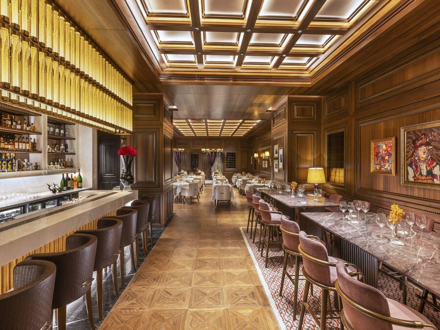 A bar area with a long counter, multiple bar stools, and a variety of bottles and glasses.