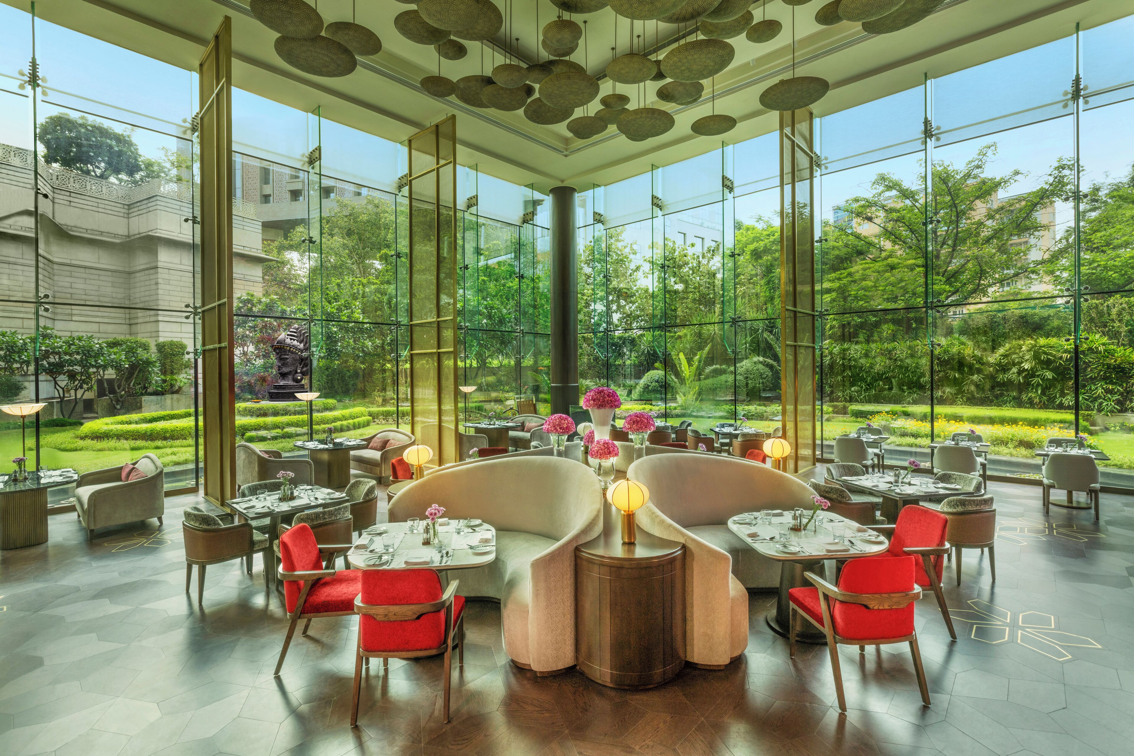 A spacious indoor dining area with large windows, modern furniture, and a view of a lush garden.