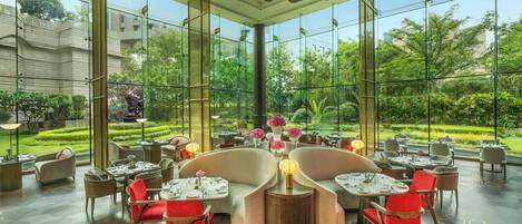 Un amplio comedor interior con ventanas grandes, muebles modernos y vistas a un jardín exuberante.