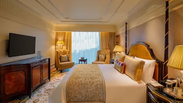 A hotel room with a large bed, two armchairs, a TV, a desk, and a window with curtains.