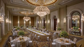 Un vaste hall de banquet doté de nombreuses tables rondes, de lustres élégants et d’un tapis à motifs.