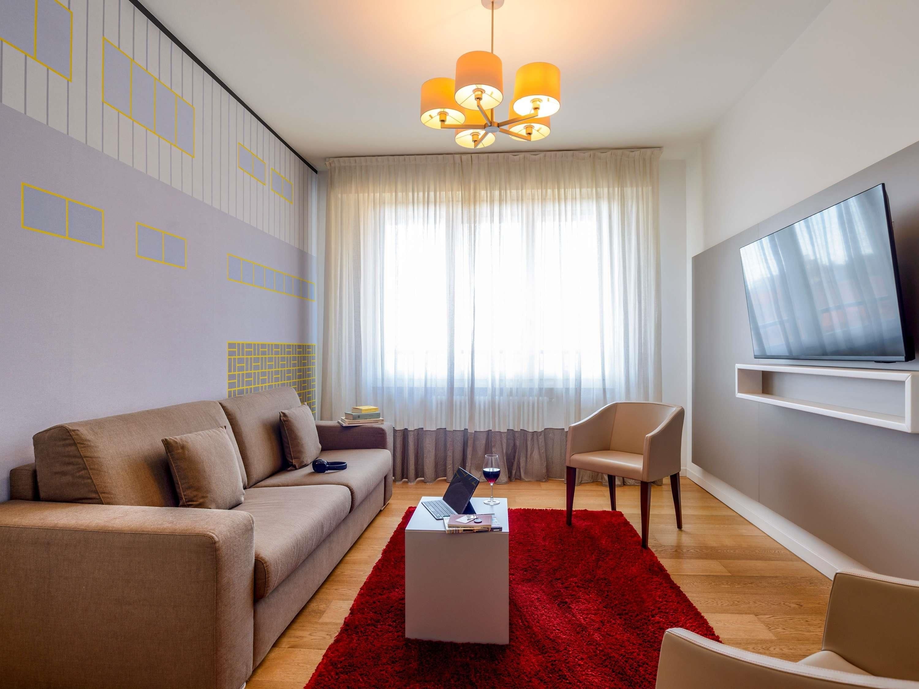 Een moderne woonkamer met een bank, fauteuil, salontafel en een aan de muur bevestigde televisie.