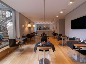 A modern hotel lobby with a bar area, wooden flooring, and a large window overlooking a staircase. - Mercure Milano Solari (Milan)