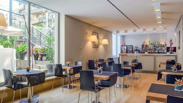 Een modern café met meerdere tafels en stoelen, een bar met een divers aanbod aan flessen, en grote ramen met uitzicht op buiten.