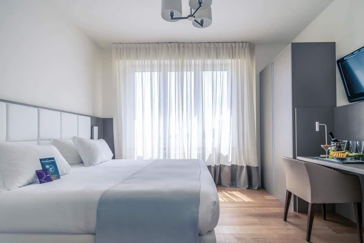 A hotel room with a bed, a desk, a television, and a window with curtains.