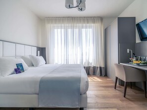 A hotel room with a bed, a desk, a television, and a window with curtains. - Mercure Milano Solari (Milan)