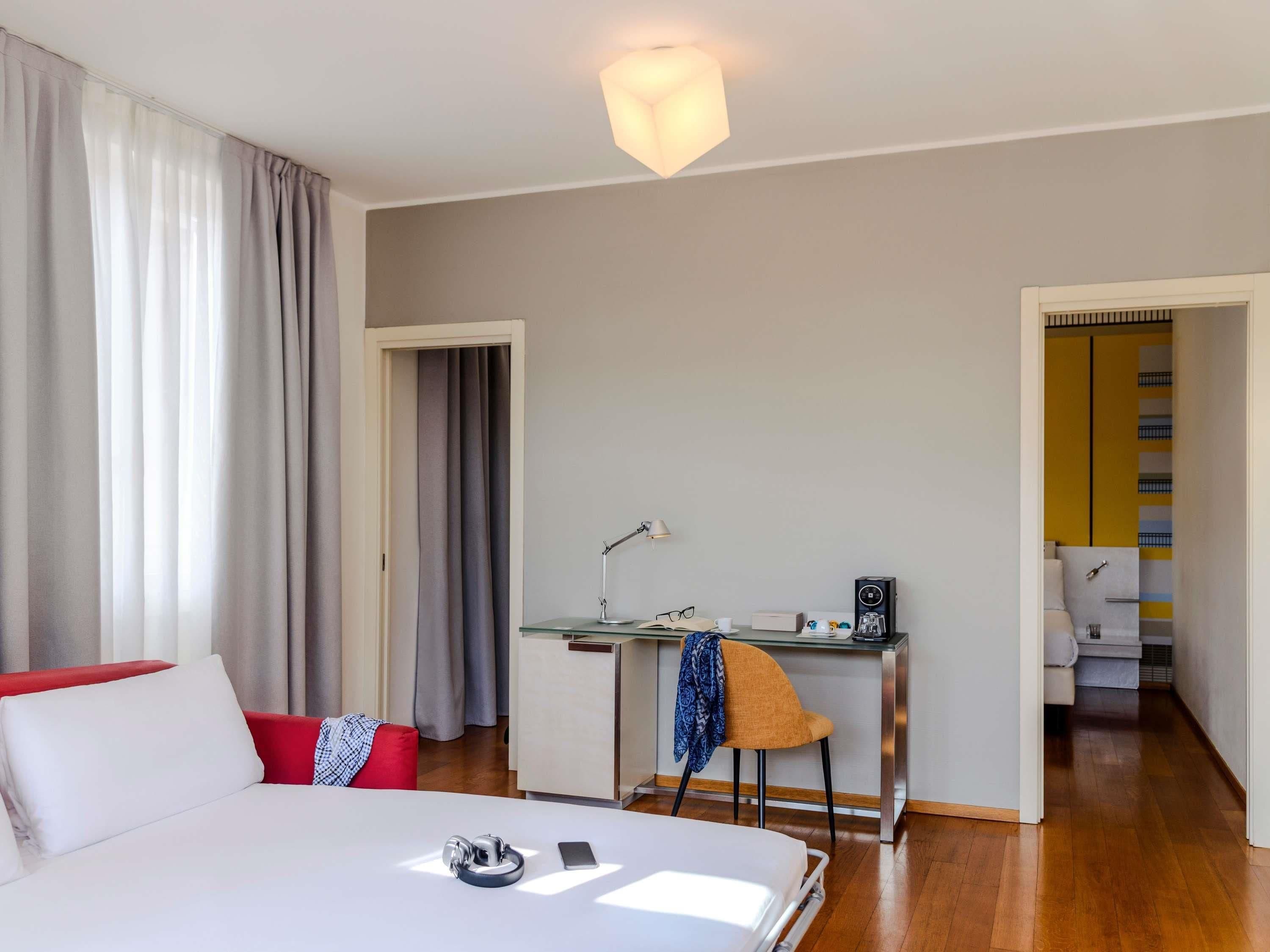 A hotel room with a bed, a desk, a chair, and a bathroom visible through an open door.