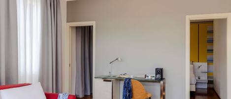 A hotel room with a bed, a desk, a chair, and a bathroom visible through an open door.