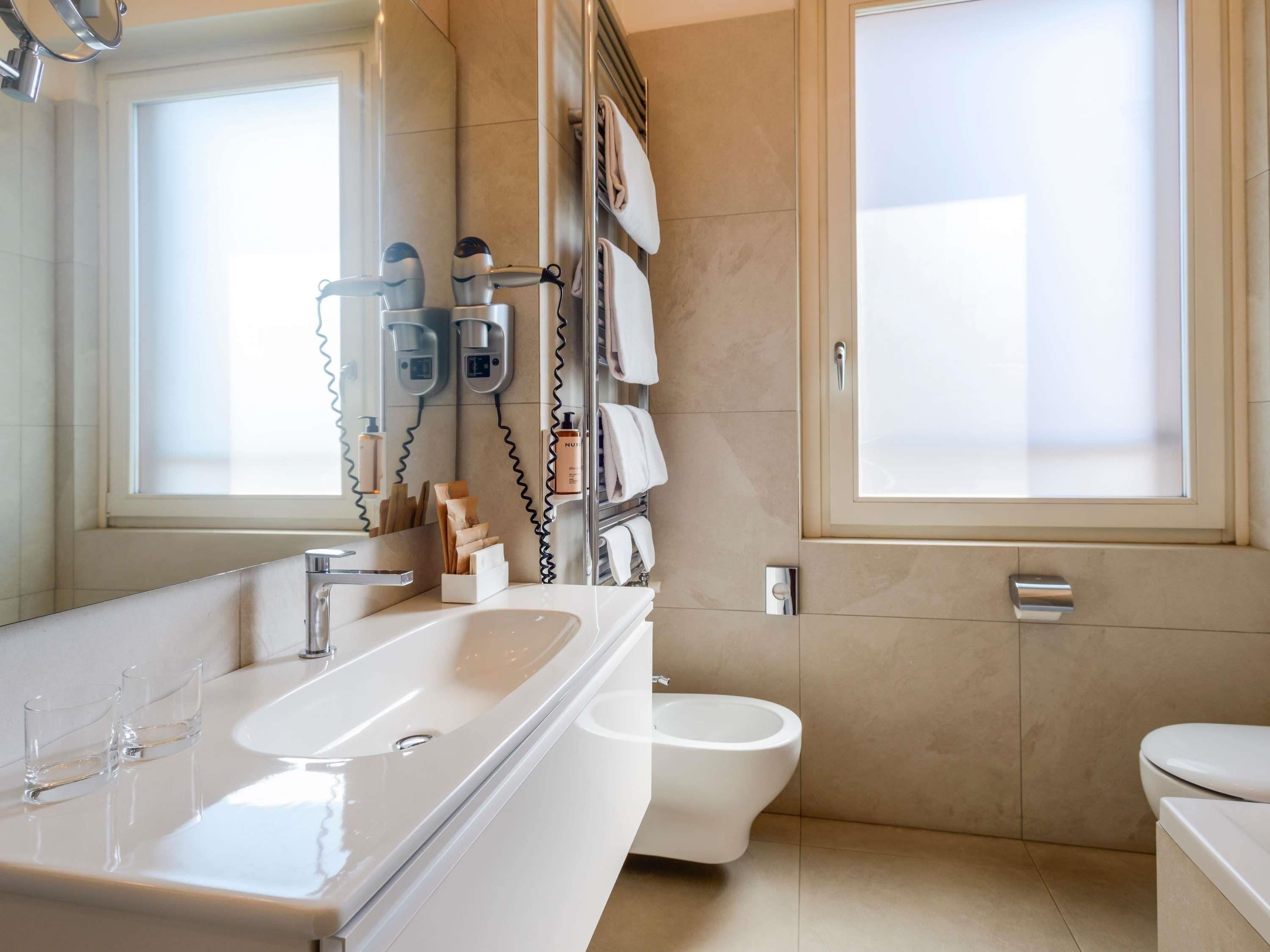 A modern bathroom with a large sink, two hair dryers, a toilet, and a mirror.