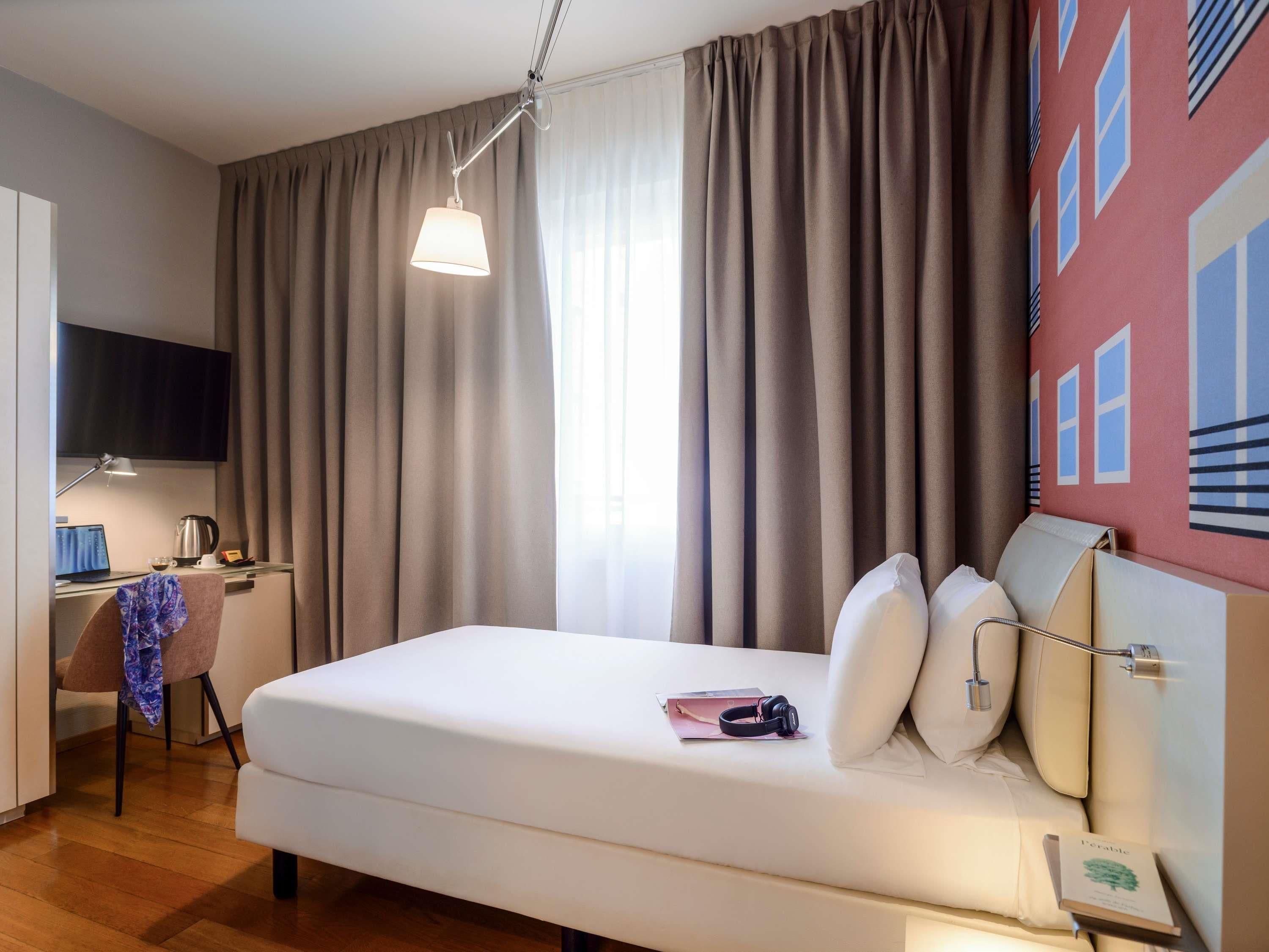 A hotel room with a bed, a desk with a computer, a chair, and a television.