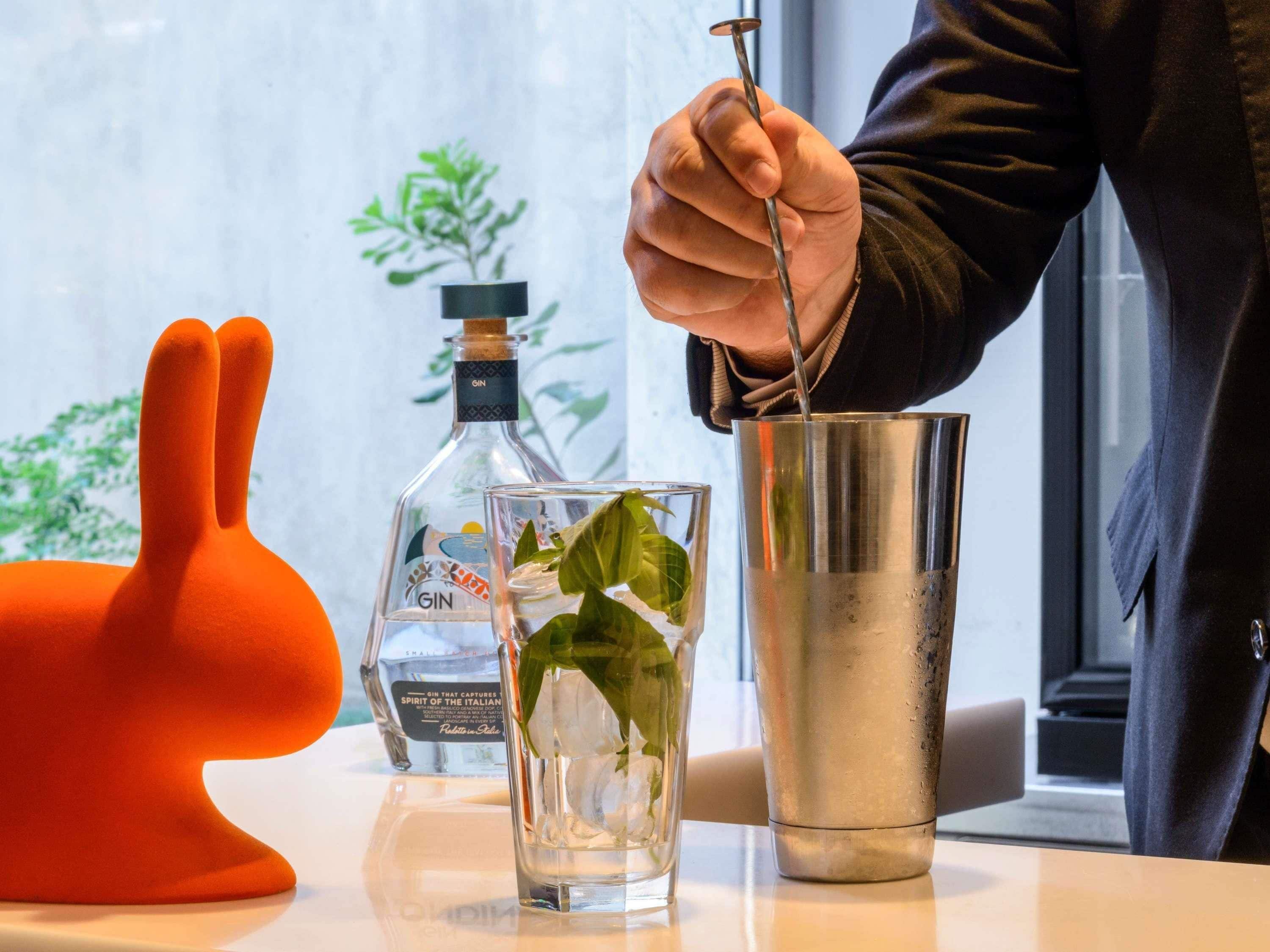 A bar setting with a cocktail shaker, a bottle of gin, and a glass with a mint leaf.