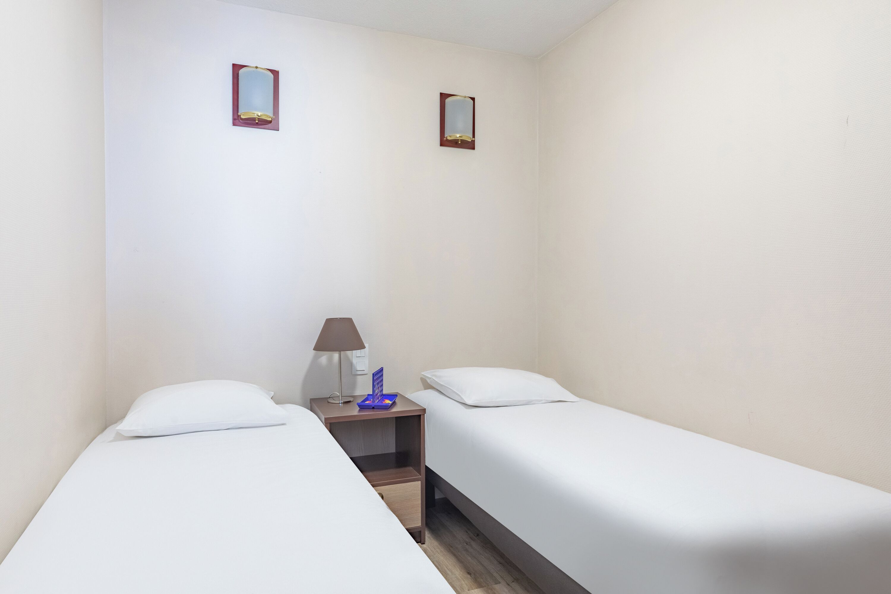 A small, clean room with two single beds, a nightstand with a lamp, and two wall-mounted mirrors.