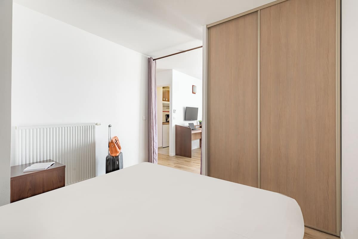 Een hotelkamer met een groot bed, een houten garderobe, een bureau met een stoel en uitzicht op de aangrenzende kamer.