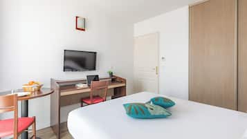 A hotel room with a bed, a desk with a computer, a chair, a television, and a wardrobe.
