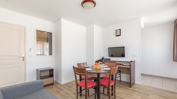 Un espace de vie compact comprenant un coin repas, un canapé, un téléviseur et une petite kitchenette.