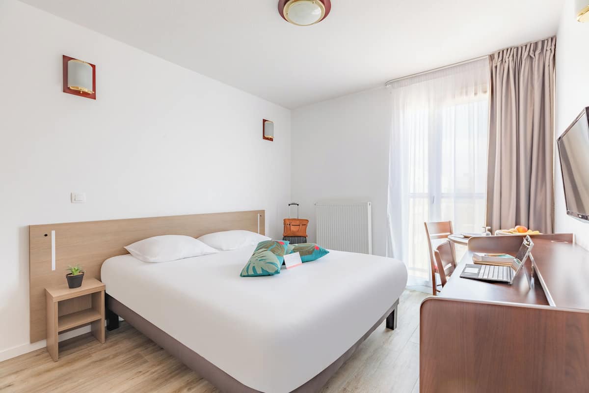 Een hotelkamer met een bed, nachtkastje, lamp en een bureau met stoel.