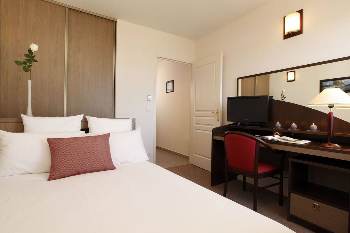Een hotelkamer met een bed, een bureau met een computer, een stoel en een bureaulamp.