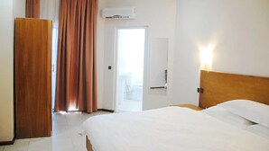 A hotel room with a bed, a wardrobe, an air conditioning unit, and a bathroom door. - Robinhood Inn (Accra)